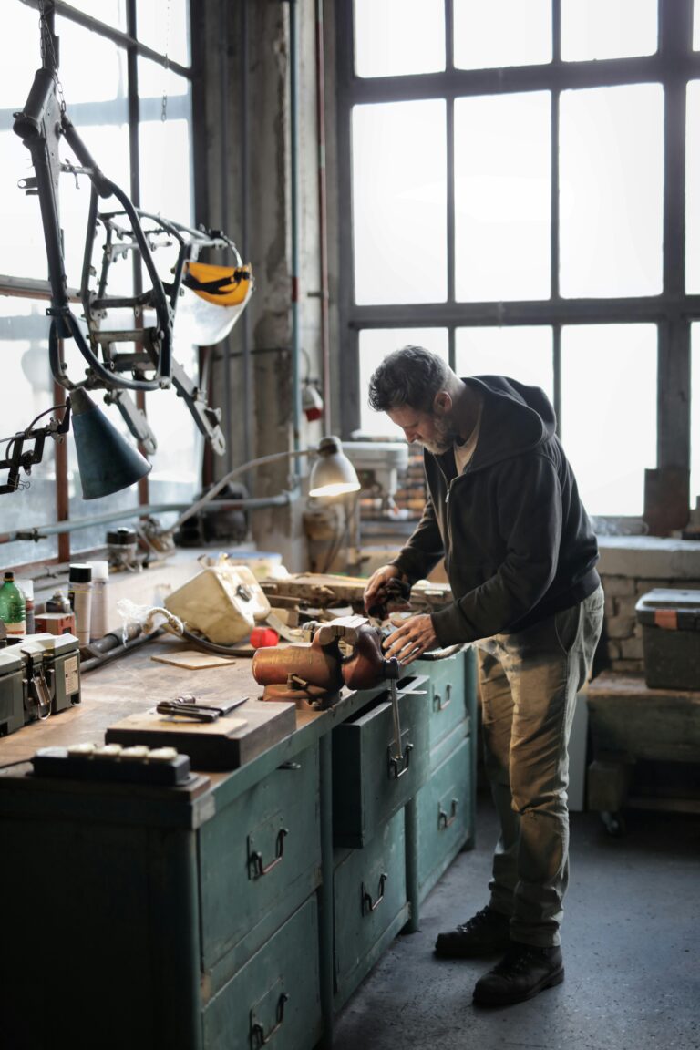 Side view of bearded male master in casual clothes standing at workbench and fixing details with professional metal instrument