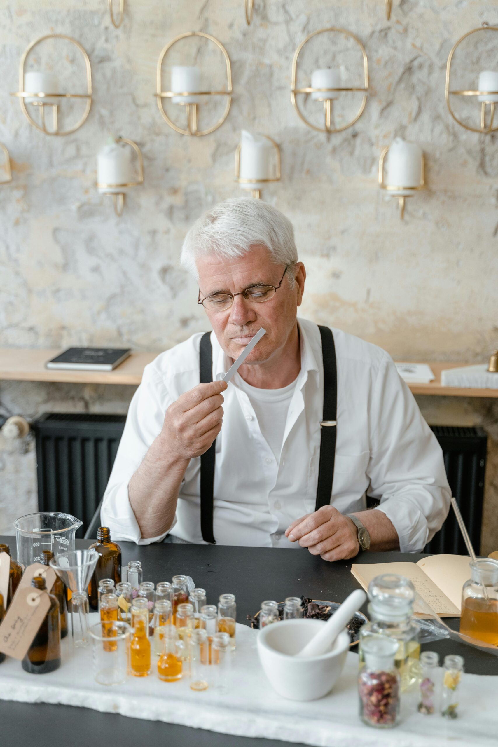 Elderly man appreciating aromatic scents in a cozy indoor setting with bottles and oils.