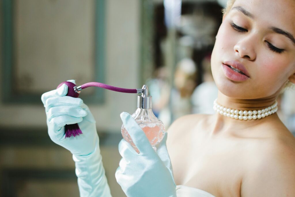 A sophisticated woman in gloves applying perfume with a traditional bottle in a vintage setting.